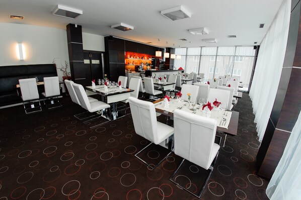 Un restaurante moderno con sillas y mesas blancas, una zona de bar y una alfombra estampada.