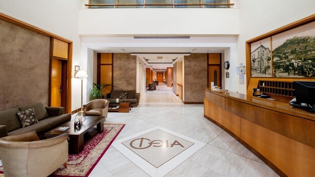 Un vestíbulo de hotel con recepción, zona de estar y un pasillo que conduce a otras habitaciones.