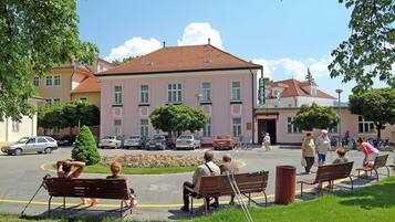 A public square with benches, a building with a red roof, and parked cars.