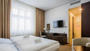 Ein Hotelzimmer mit zwei Betten, einem Schreibtisch, einem Sessel, einem Fernseher und einer Tür zu einem weiteren Raum.
