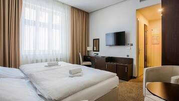 A hotel room with two beds, a desk, a chair, a TV, and a door leading to another room.