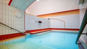 A swimming pool with a tiled floor and walls, a red and white color scheme, and a handrail.