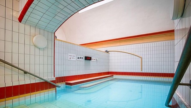 Una piscina con paredes de azulejos y un borde rojo, una barandilla y un cartel que indica la profundidad de la piscina.