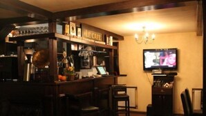Eine Bar mit einer Theke, Barhocker, einem an der Wand montierten Fernseher und einer Kandelaber.