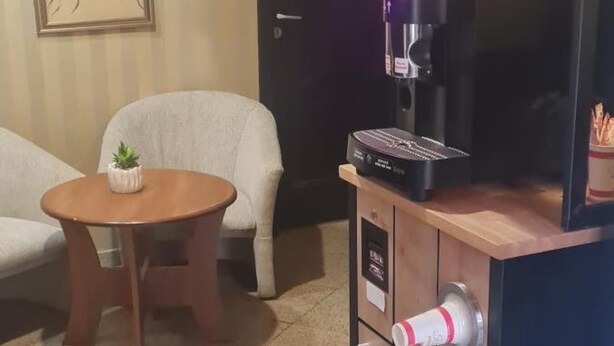 Ein Zimmer mit Kaffeemaschine, einem kleinen Tisch mit Pflanze und zwei Stühlen.