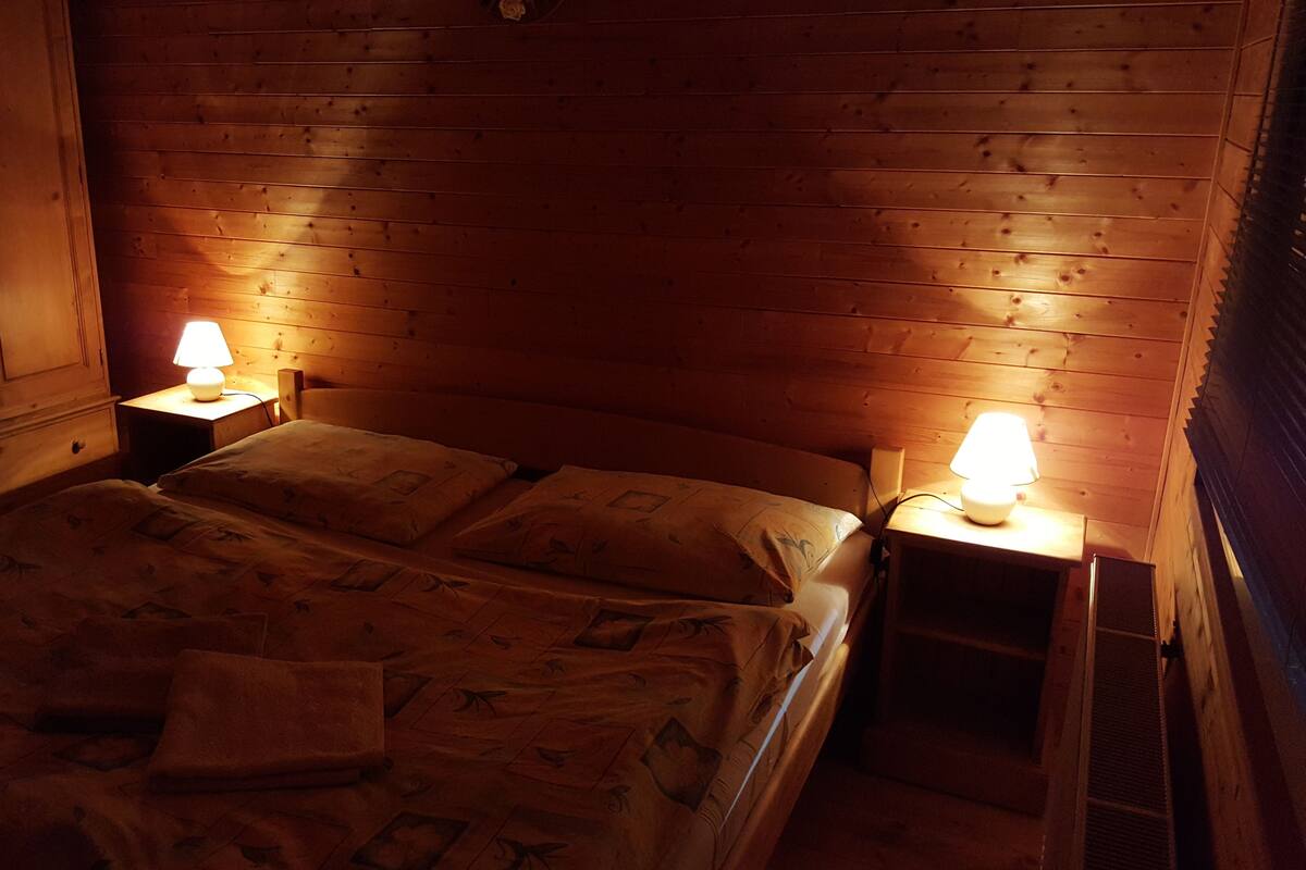 A cozy wooden room with a bed, two bedside tables with lamps, and a wardrobe.