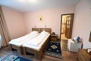 Cama doble con cabecera de madera, mesita de noche con teléfono, un refrigerador pequeño y puerta que da a un baño.