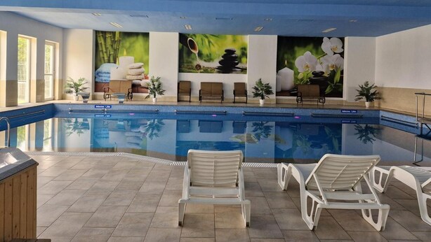 Une piscine avec des chaises longues, un espace spa doté d’un bain en pierre, et une vue sur l’extérieur.