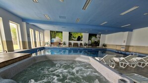Un bain à remous agrémenté d’une cascade, entouré de chaises longues et d’une piscine.