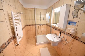 Baño de hotel con cabina de ducha de vidrio, lavamanos y toallero.