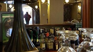 Un coin bar agrémenté d’un grand miroir, d’un chandelier et de différentes bouteilles de spiritueux.