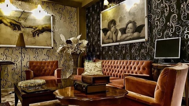 Un salon avec un canapé capitonné, une table basse sur laquelle sont posés des livres, un vase rempli de fleurs et deux œuvres d’art encadrées accrochées au mur.