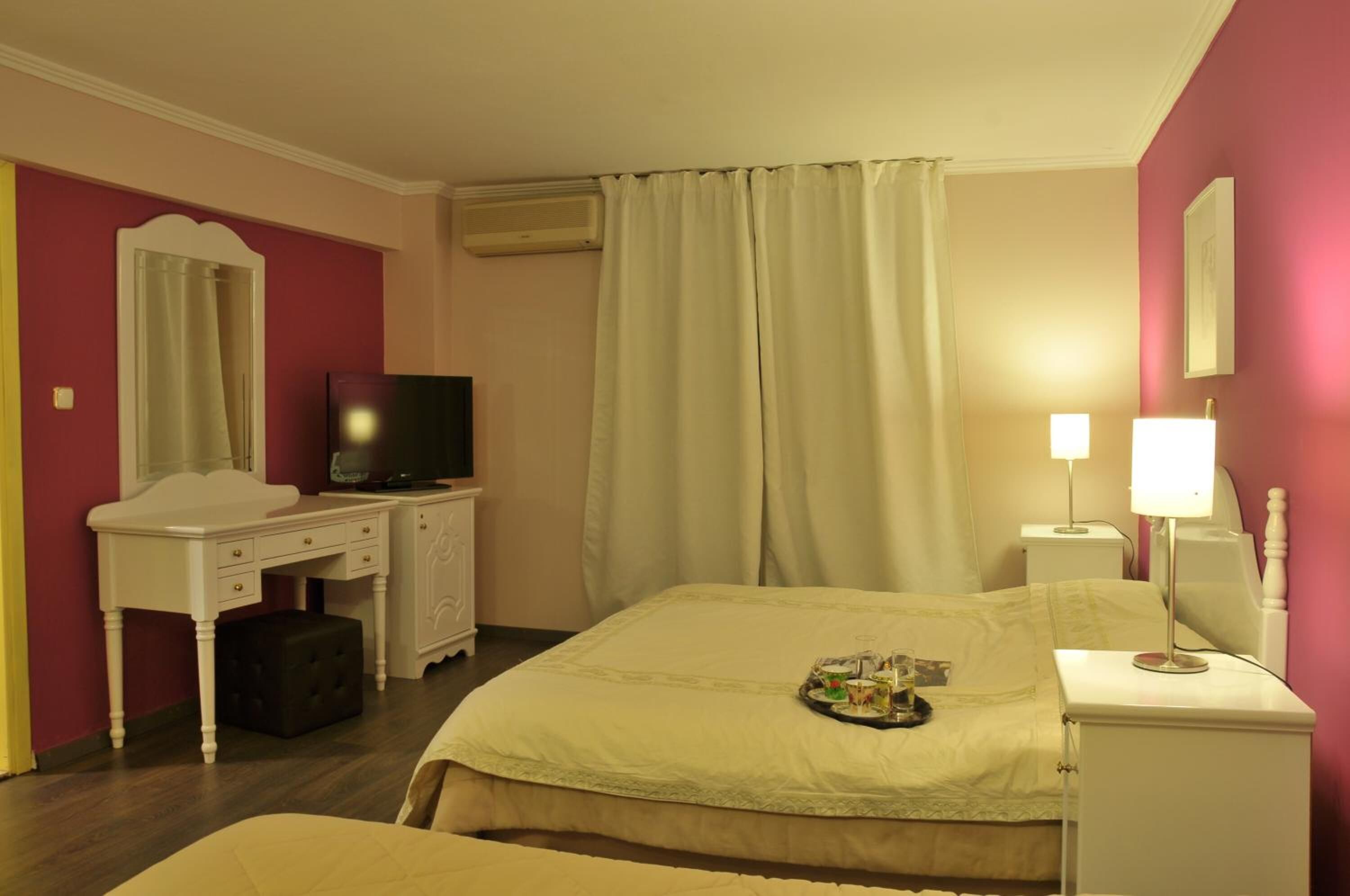 A hotel room with a bed, a desk with a television, a lamp, and a tray with items on the bed.