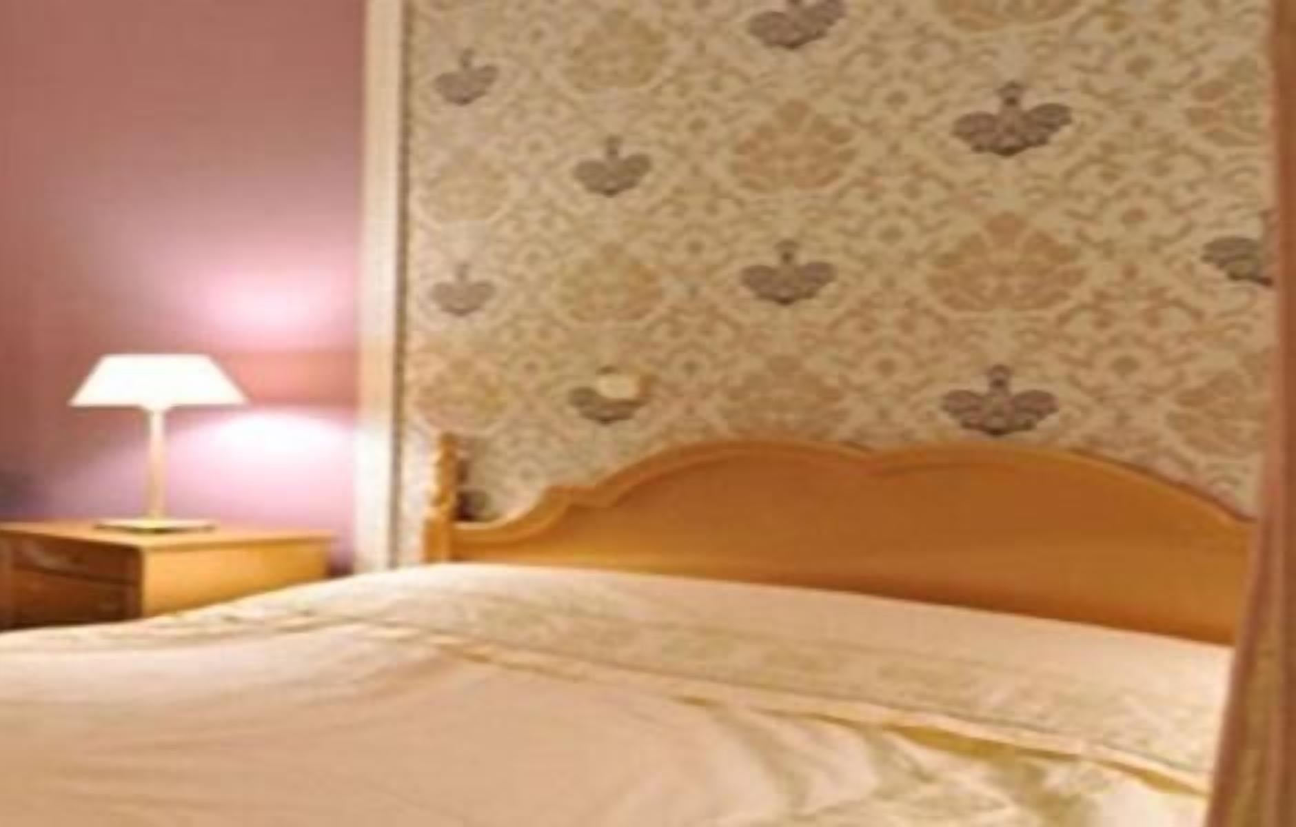 A bedroom with a wooden headboard, a bedside table with a lamp, and patterned wallpaper.