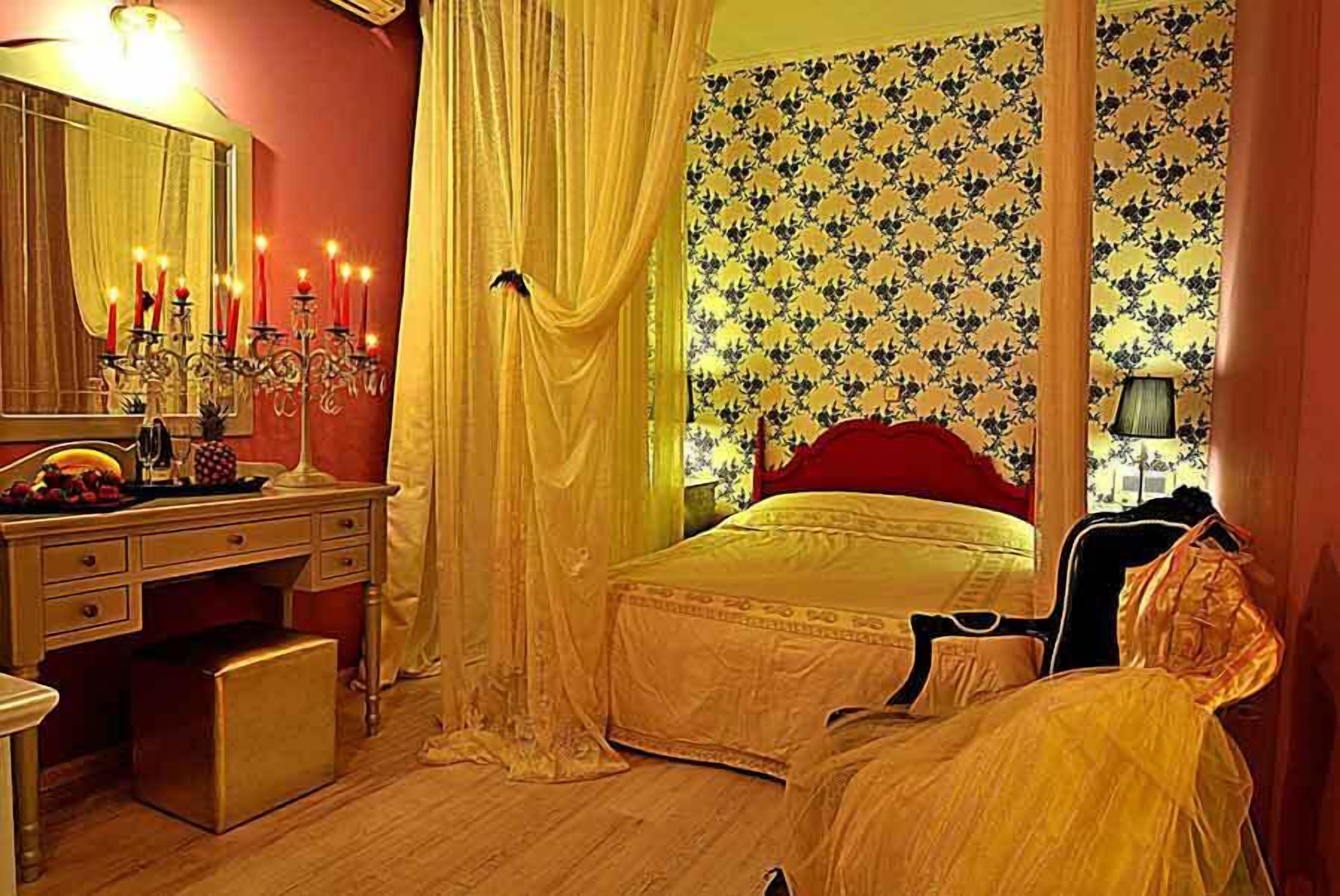 A bedroom with a bed, a desk, a mirror, and a dresser.