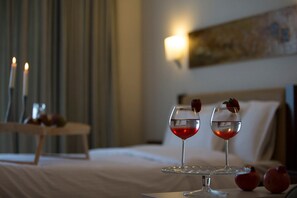 A hotel room with a bed, a bedside table with candles, and two glasses of red drink with strawberries on a coaster. - Hotel Zefyros (Dio-Olympos)
