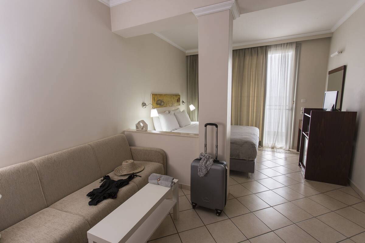 Habitación de hotel con sofá, una mesita, maleta, cama, escritorio y espejo.