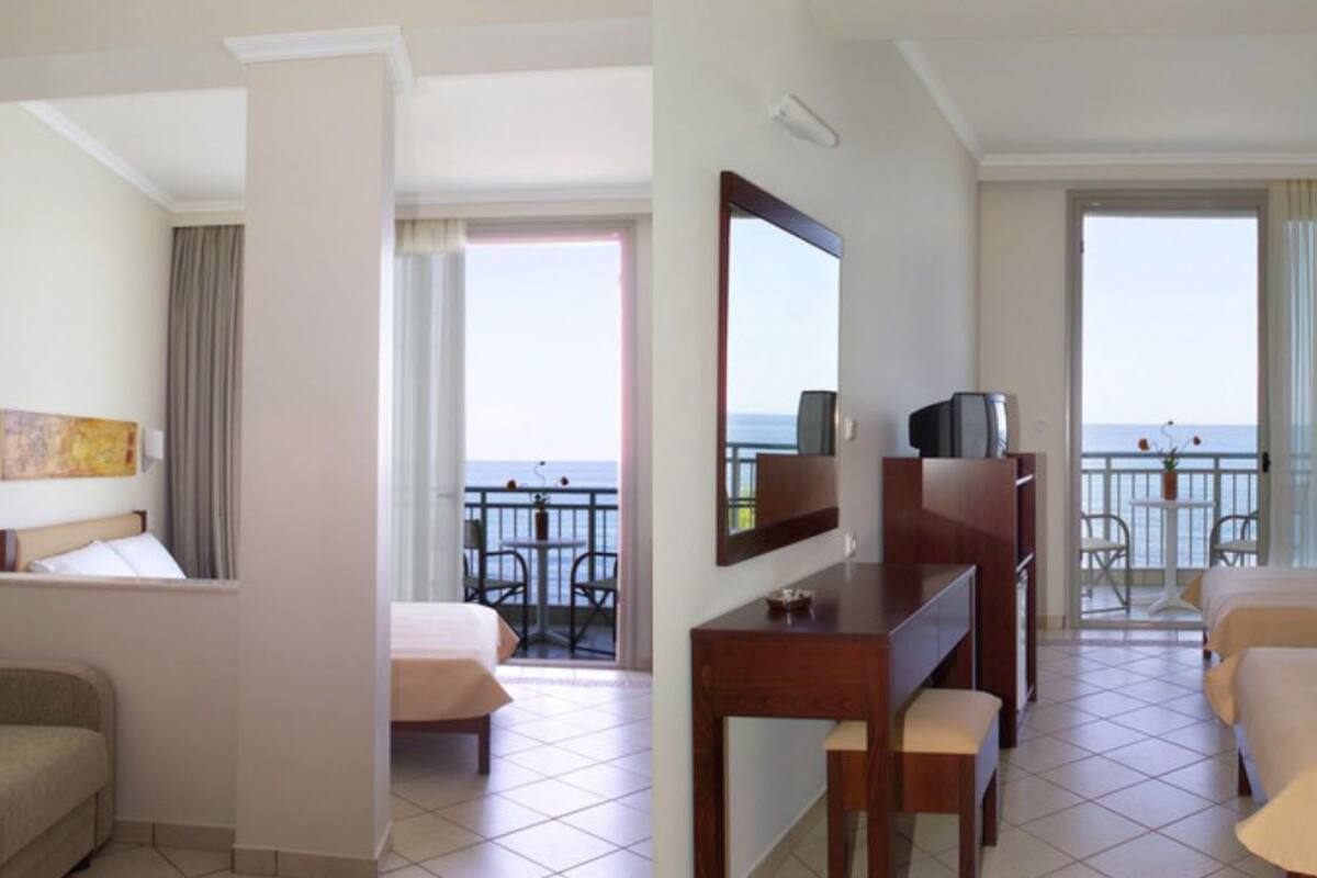 Habitación de hotel con cama, escritorio, silla, televisor y balcón con vista al mar.