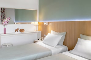 Hotelkamer met twee bedden, een nachtkastje met lamp, een spiegel en een klein schapje met decoratieve objecten.