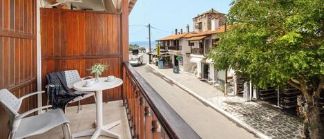 A balcony with a table and chairs, overlooking a street with buildings and a tree.