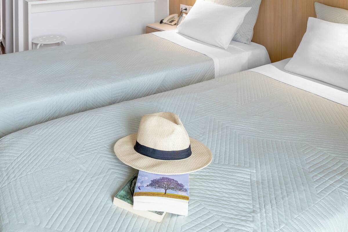 A hotel room with two beds, a desk with a lamp, a mirror, and a small wooden cabinet.