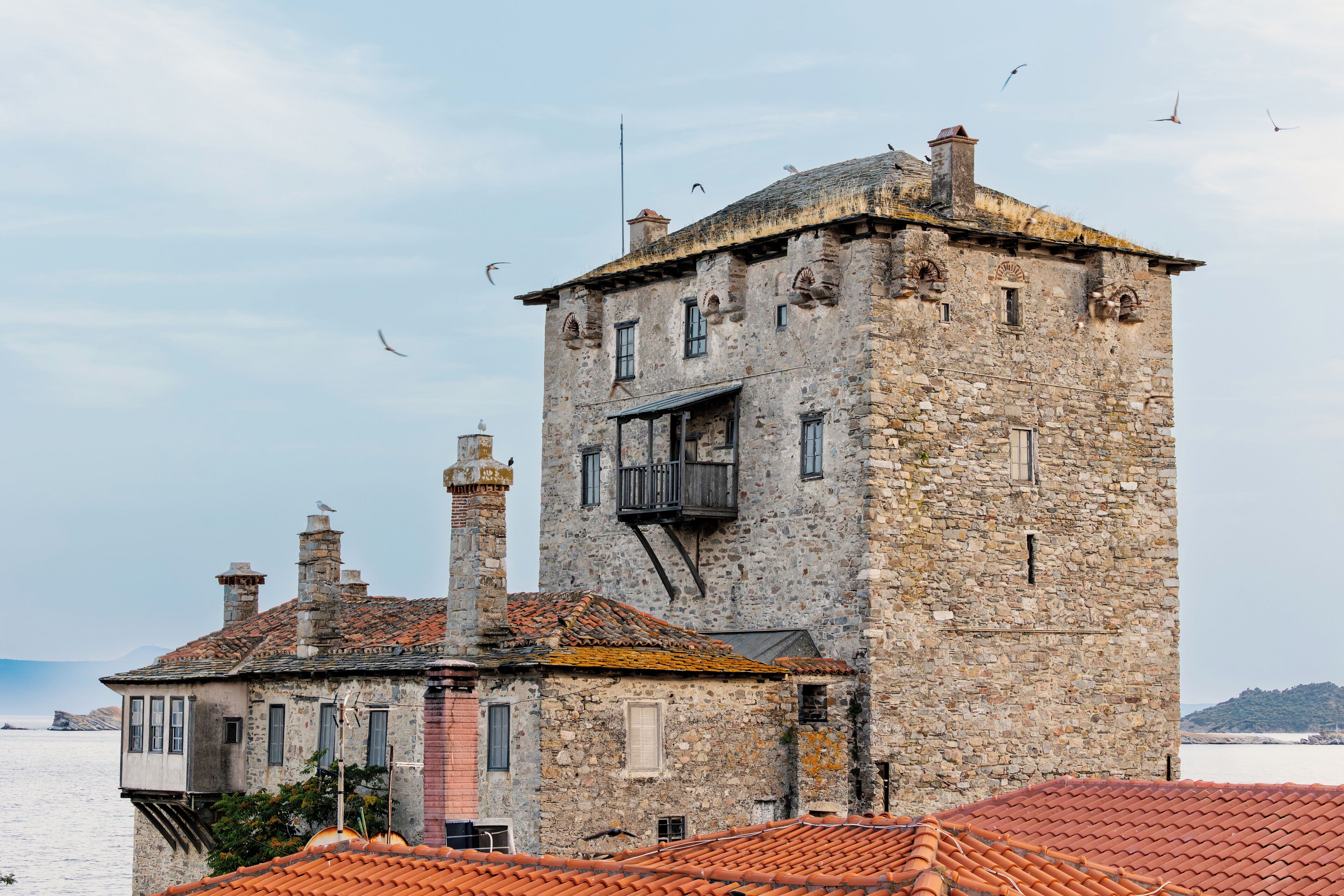 Un edificio de piedra con balcón, tejado de tejas y vista al mar.