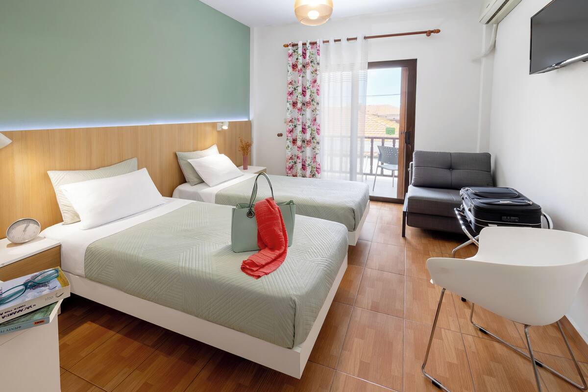 A hotel room with two beds, a chair, a desk, and a TV.