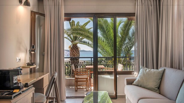 A modern hotel room with a balcony, a sofa, a dining area, and a kitchen. - Hotel Pyrgos Boutique & Suites (Aristotelis)