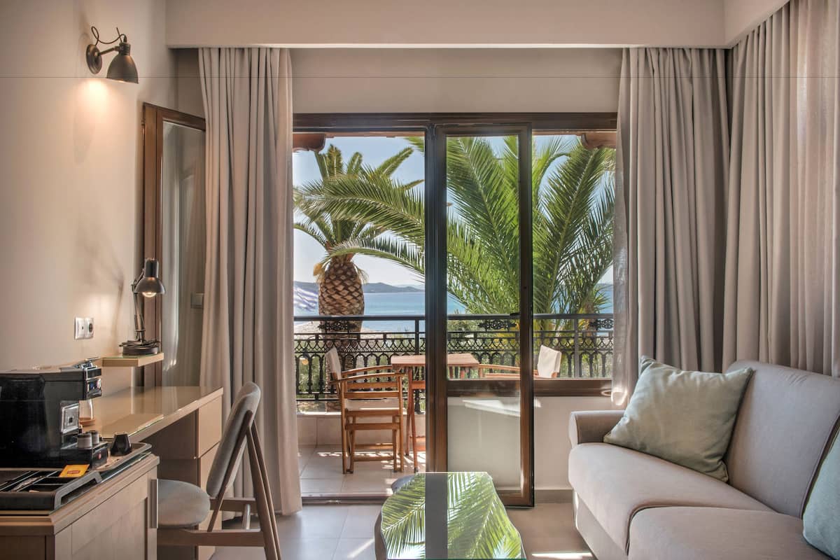 A modern hotel room with a balcony, a sofa, a dining area, and a kitchen.