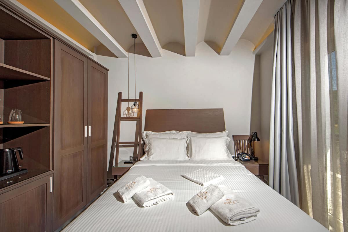 A hotel room with a large bed, wooden wardrobe, a nightstand, and a desk with a lamp.