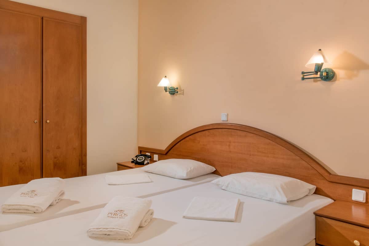 A hotel room with two beds, wooden headboards, white linens, and wall-mounted nightstands with lamps.