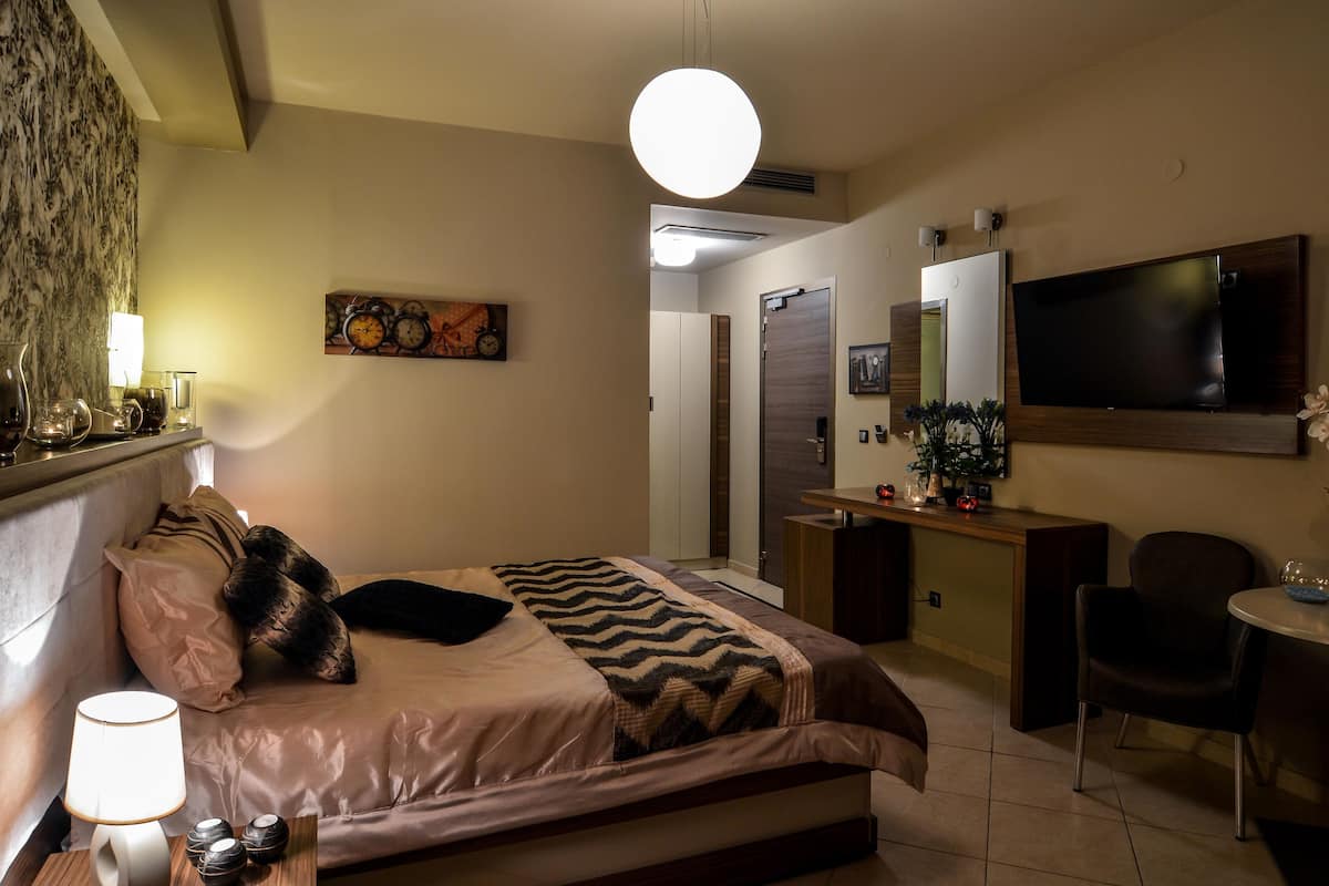 Quarto com cama, mesa de cabeceira, abajur e televisão.