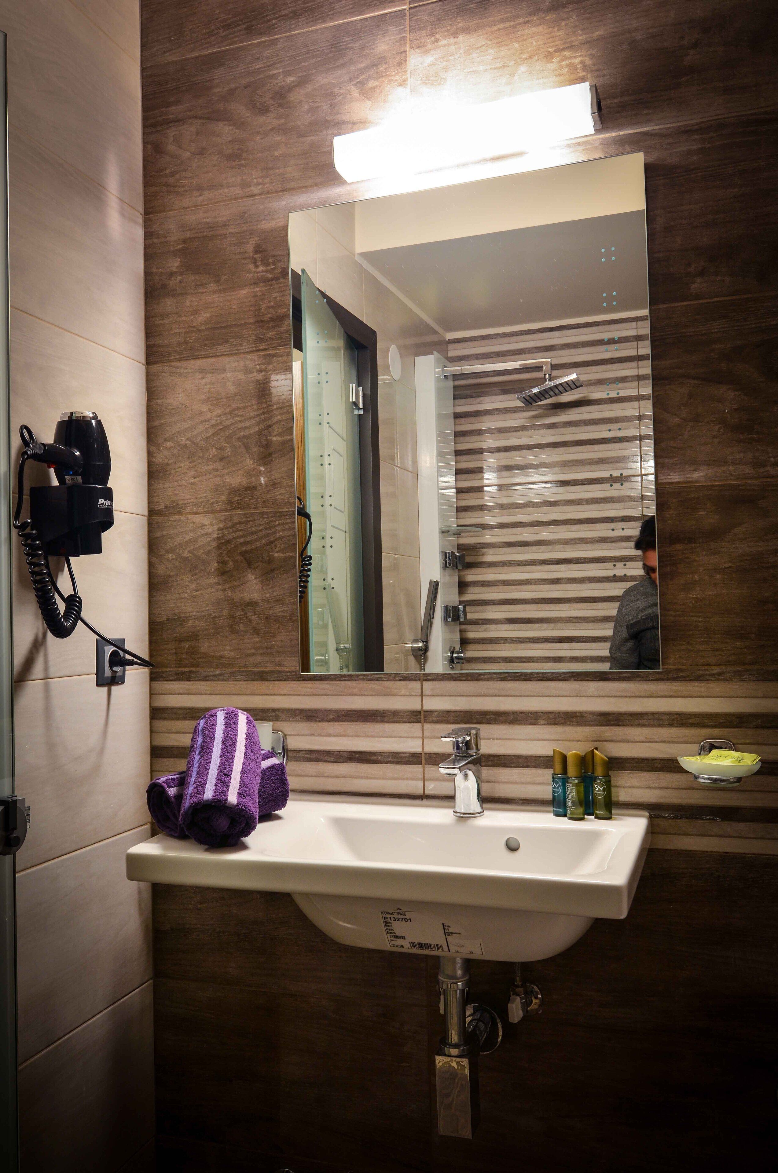 A bathroom with a sink, mirror, hairdryer, and towel rack.