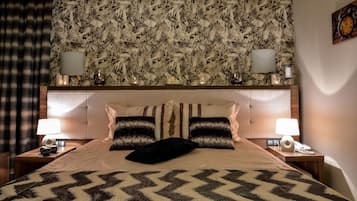 A hotel room with a large bed, two bedside lamps, a floral-patterned headboard, and a clock on the wall.