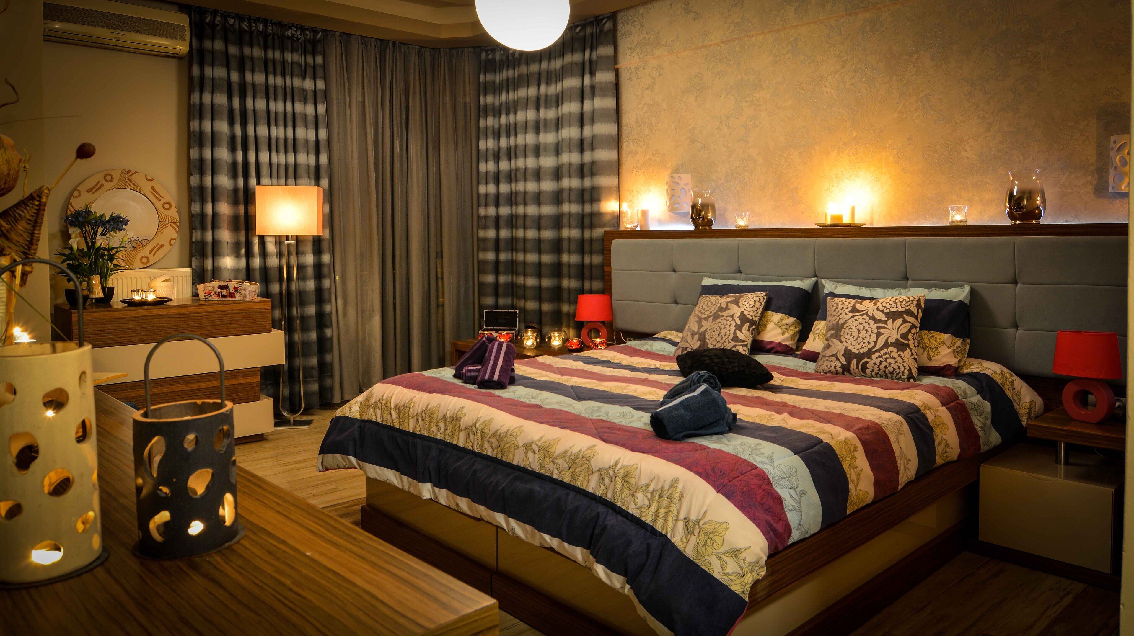 Een keurig opgemaakt slaapkamer met een groot bed, nachtkastjes, een lamp en een wandairconditioner.