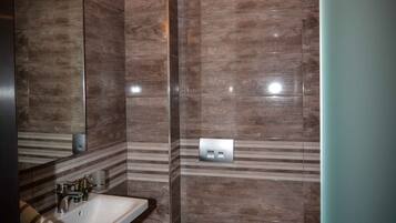 A modern bathroom with a sink, mirror, toilet, and trash can.