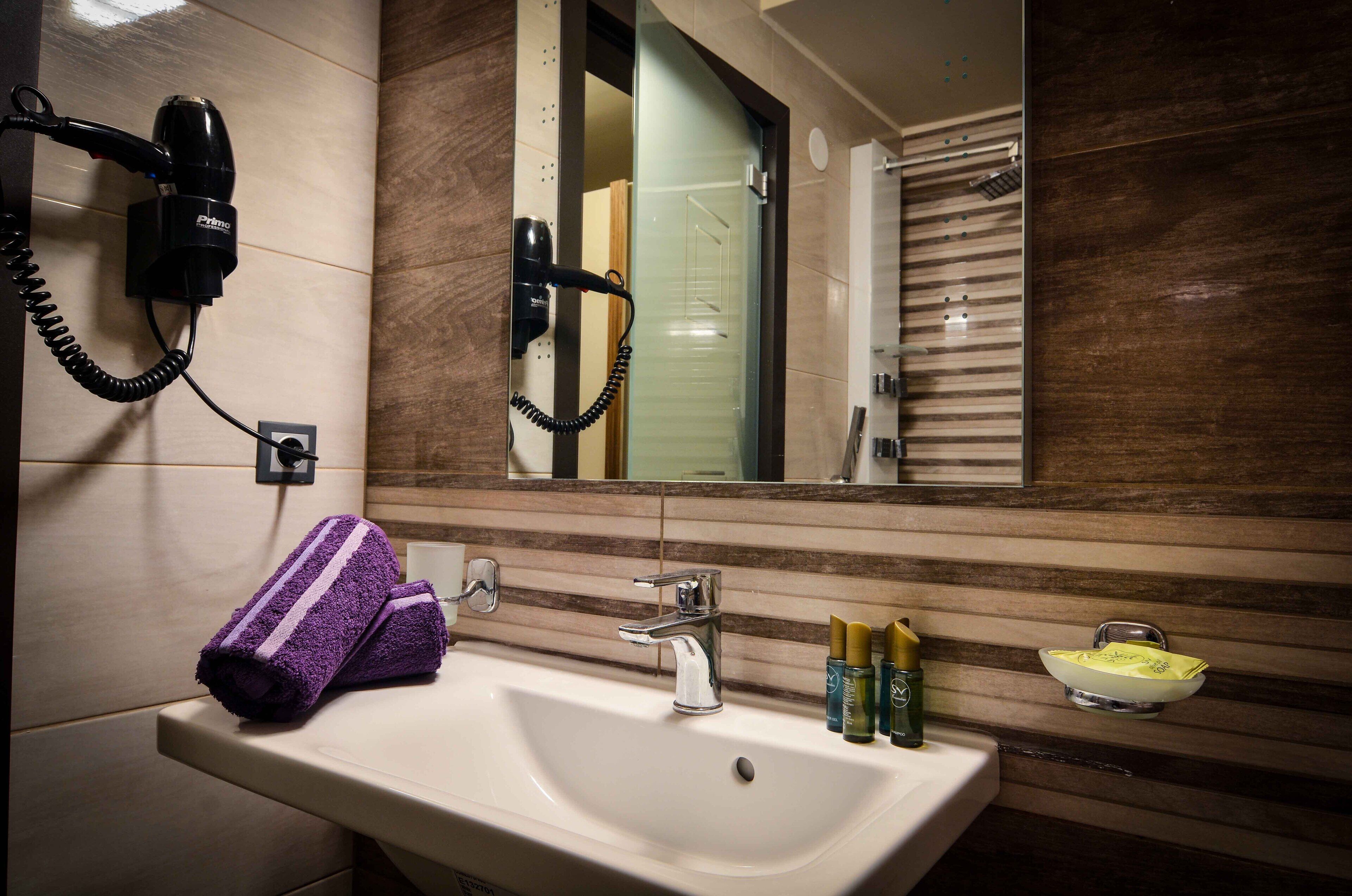 A bathroom with a sink, mirror, hairdryer, and toiletries.