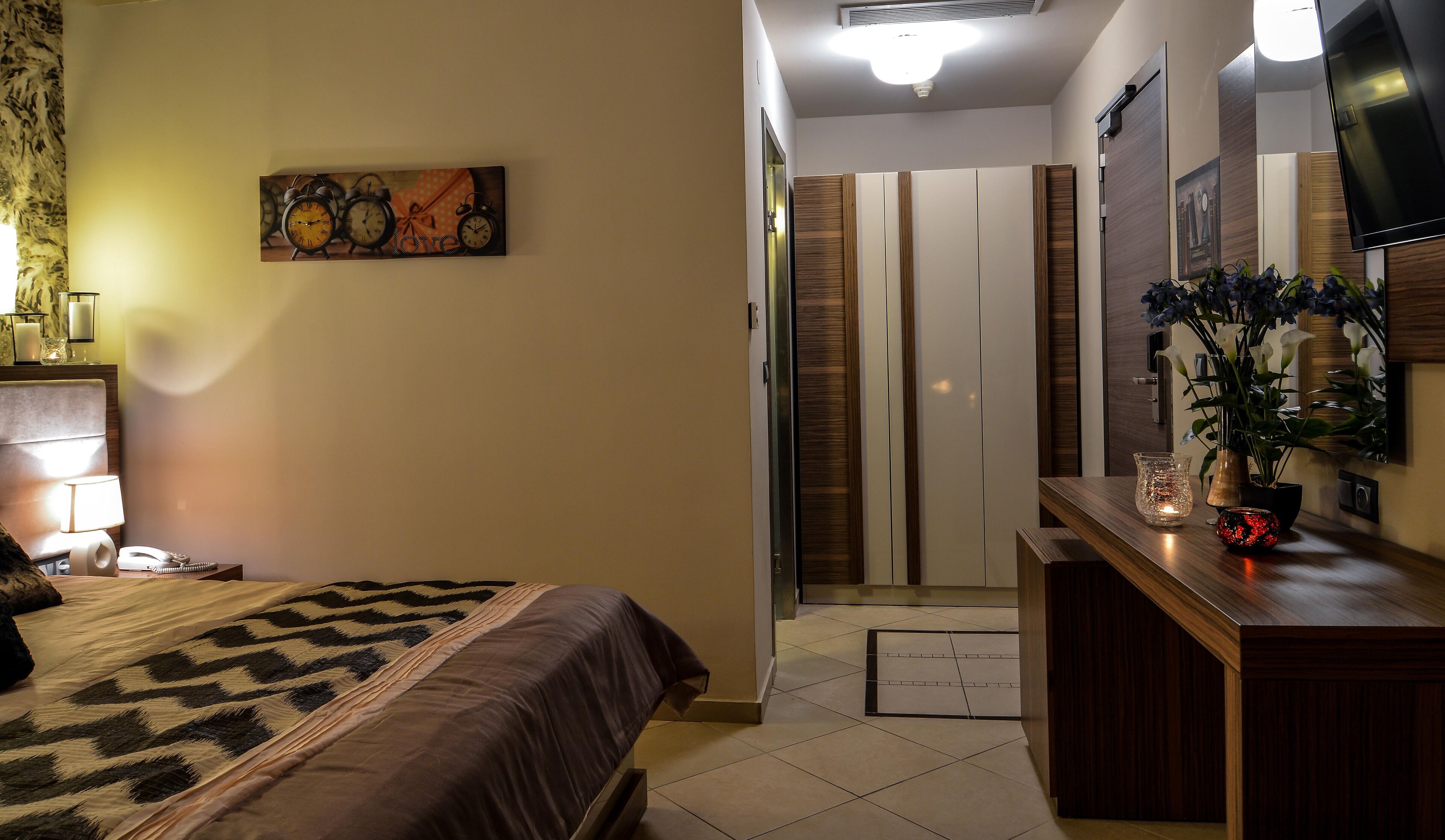 A hotel room with a bed, bedside table, lamp, and a painting on the wall.