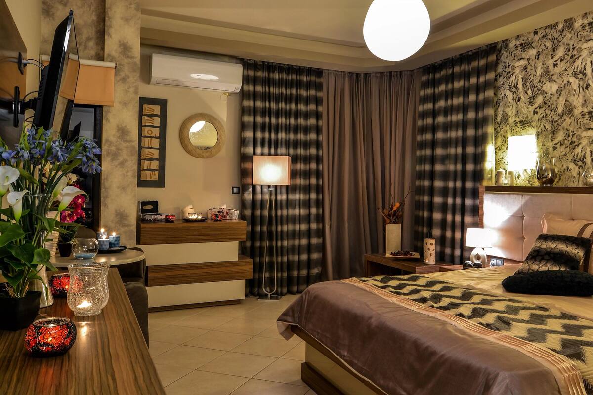 Quarto de hotel com cama, mesa de cabeceira, abajur e um espelho grande.