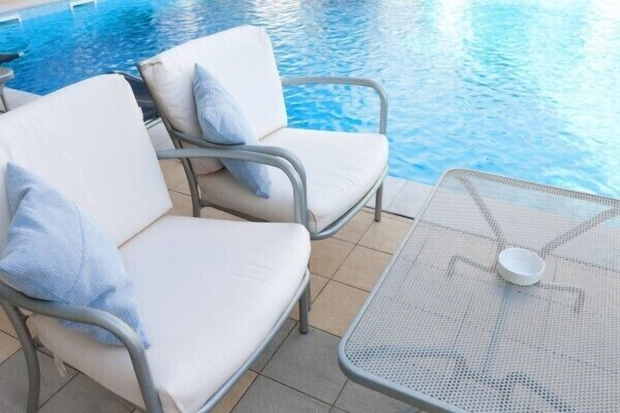 Een zwembadgedeelte met twee witte fauteuils en een metalen tafel met een schaal.