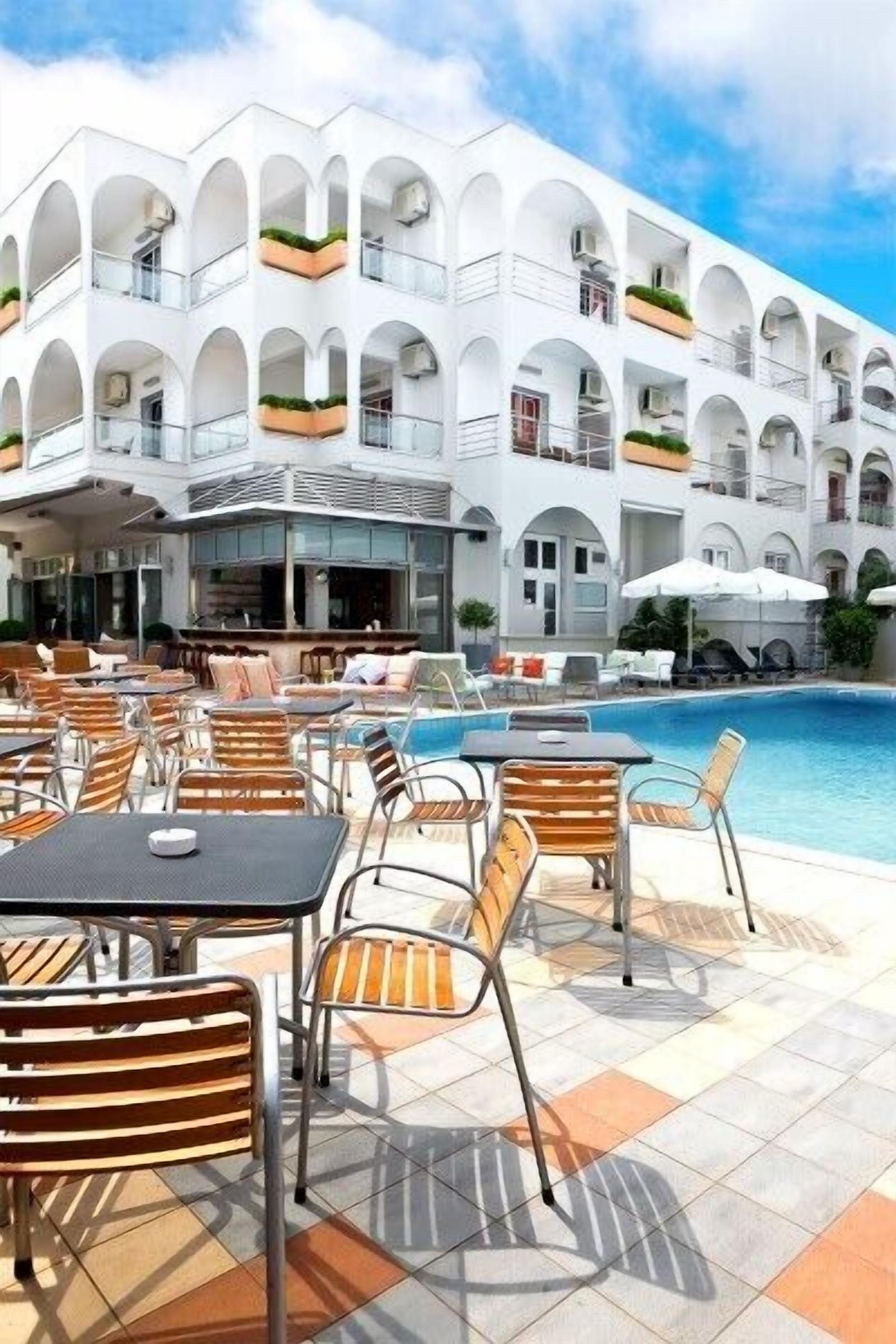 A hotel with a pool area, outdoor seating, and a white building with multiple balconies.