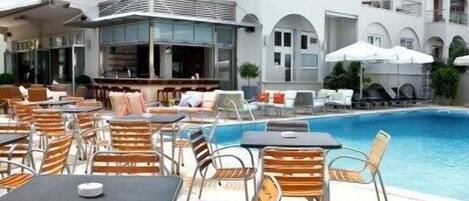 A hotel with a pool area, outdoor seating, and a white building with multiple balconies.