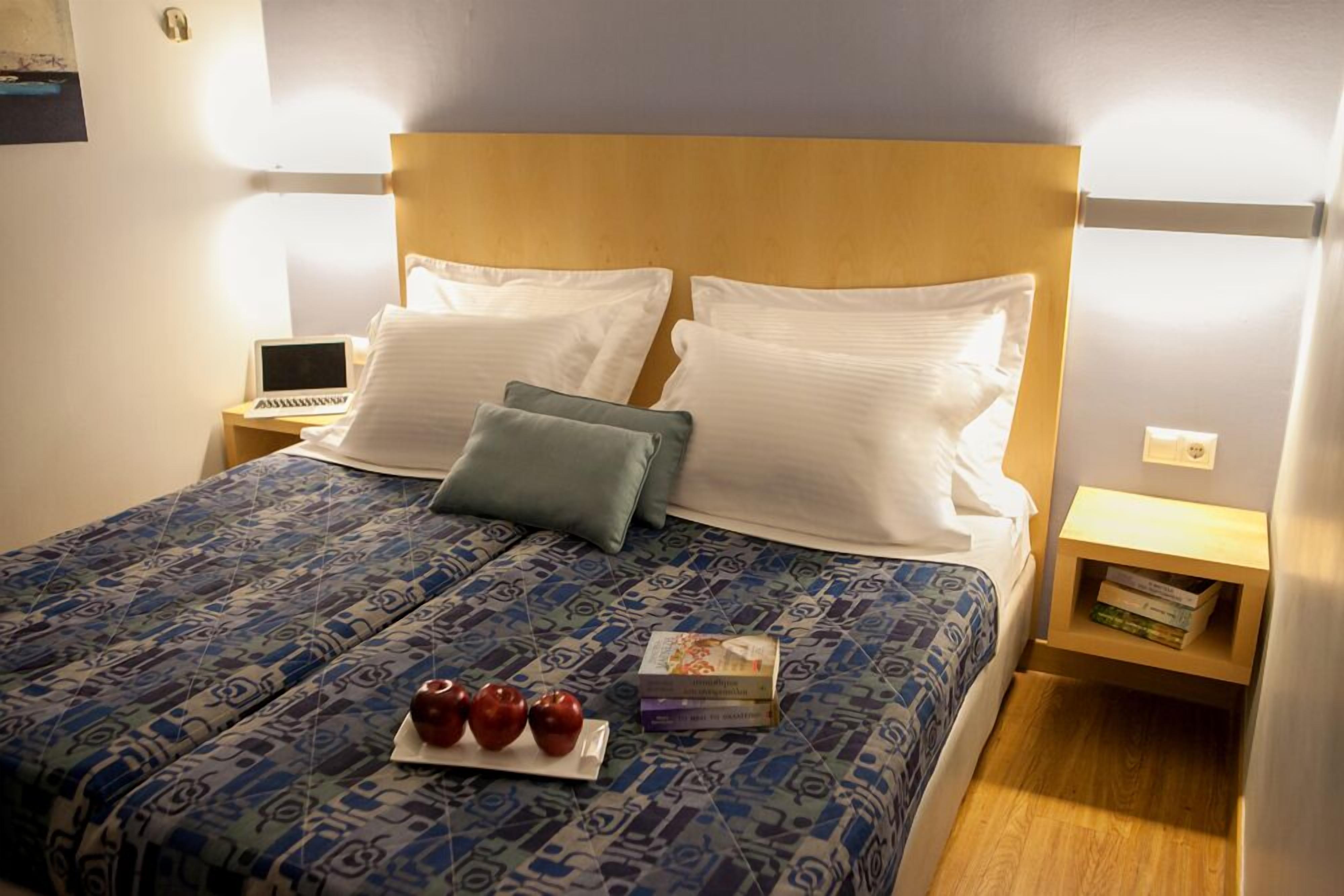 A neatly made bed with a patterned bedspread, two pillows, and a bedside table with a laptop and books.