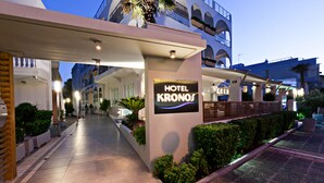 Een hotelentree met een bord waarop 'HOTEL KRONOS' staat, een overdekte doorgang en een goed onderhouden tuin.