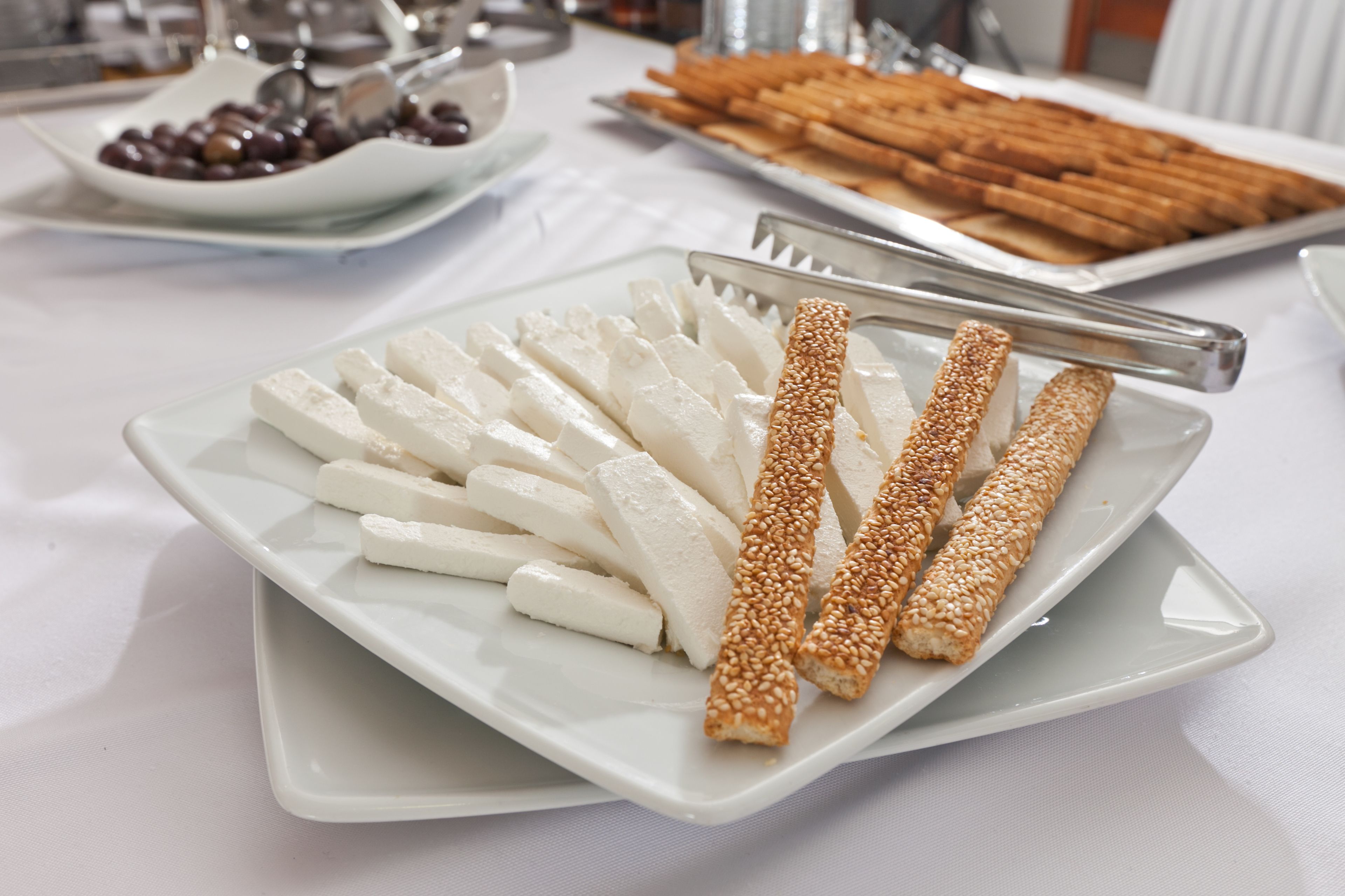 Una mesa de buffet con diversos alimentos, incluyendo rebanadas de queso blanco y palitos de pan cubiertos de sésamo.