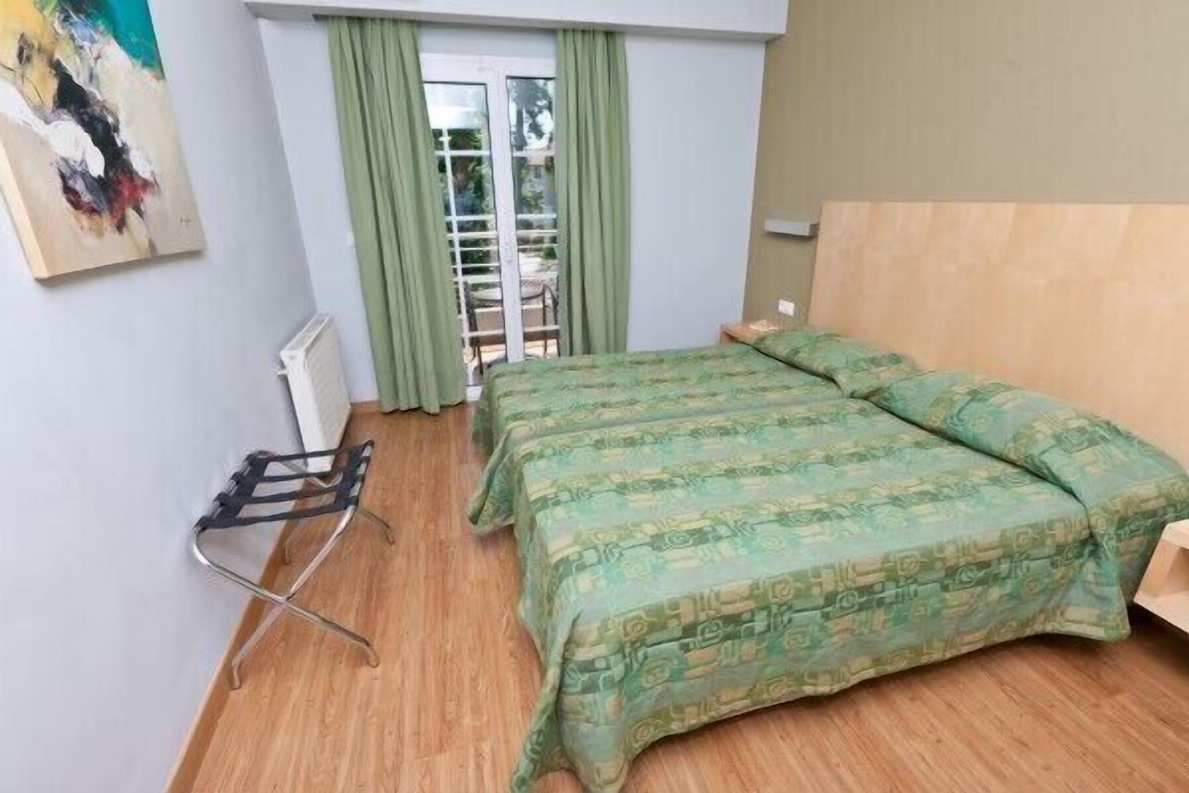 Habitación de hotel con cama, radiador, tendedero y vistas al exterior a través de una ventana con cortinas.