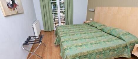 Habitación de hotel con cama, radiador, tendedero y vistas al exterior a través de una ventana con cortinas.