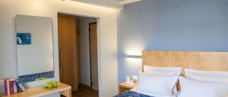 Una habitación de hotel con una cama, una mesita de noche y un escritorio con un espejo. Hay una bandeja con alimentos para el desayuno sobre la cama.