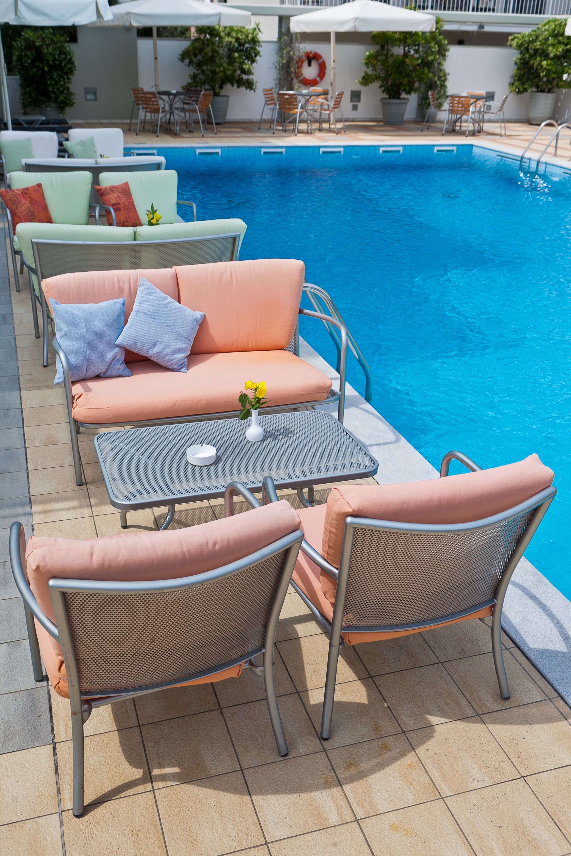 A poolside area with lounge chairs, a table, and a small table with a vase of flowers.
