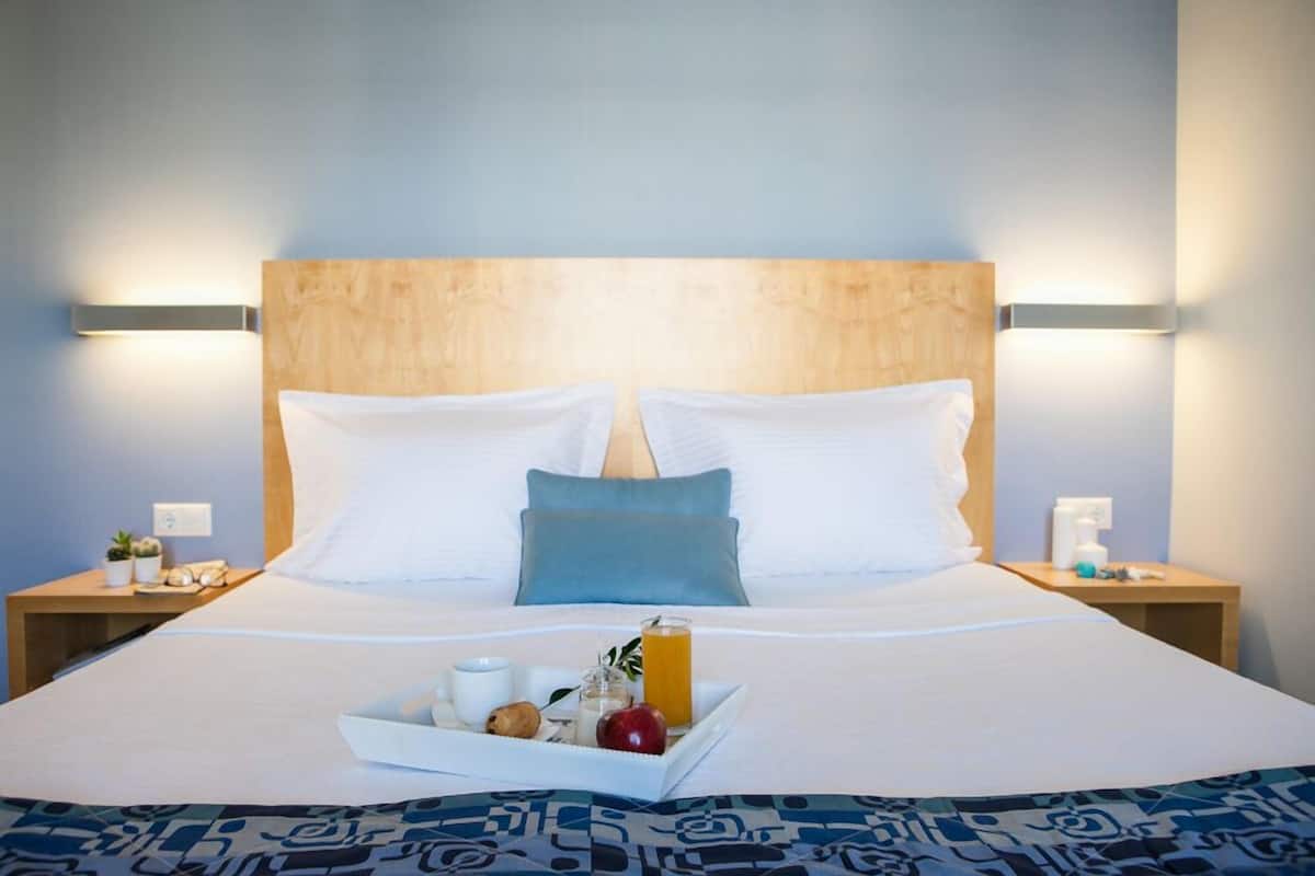 A neatly made bed with white linens, a tray of breakfast items, and a blue pillow.